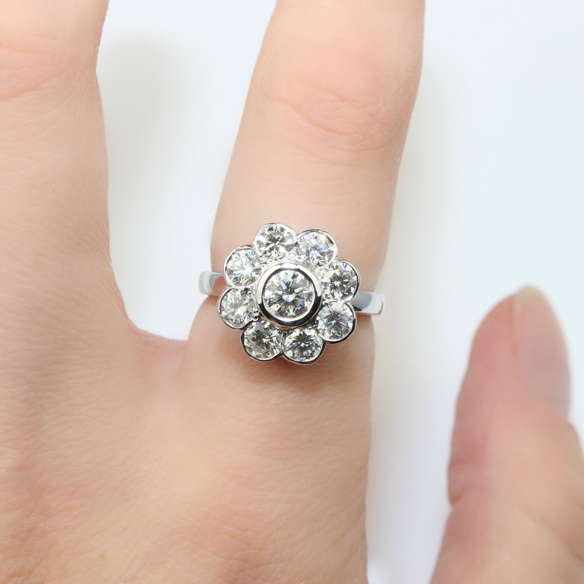 A silver-toned flower ring with clear round-cut gemstones, shown worn on a person's finger against a plain white background.